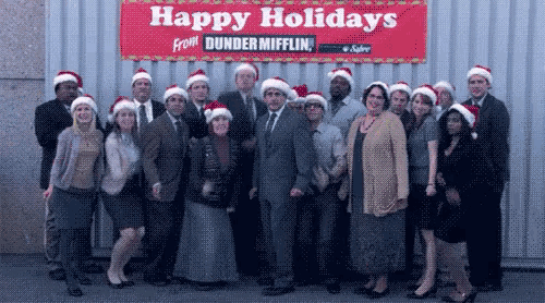 a group of people wearing santa hats are posing in front of a sign that says happy holidays from dunder mifflin