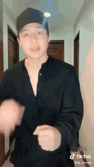 a young man wearing a black shirt and a hat is dancing in a hallway .