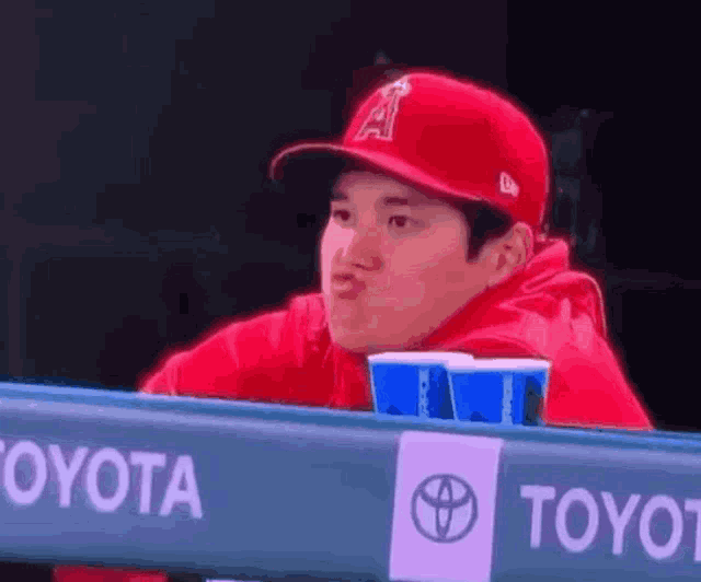 a man wearing a red hat with the letter a on it is sitting at a toyota sign
