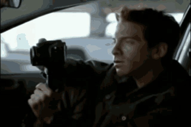 a man in a car is holding a camera in his right hand