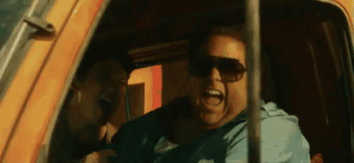 a man wearing sunglasses is sitting in a car and screaming .