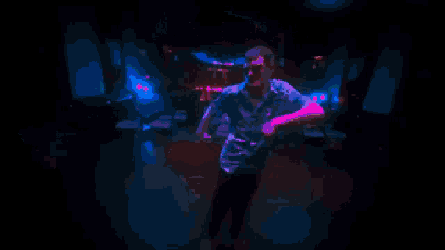 a man in a blue shirt dancing in a dark room