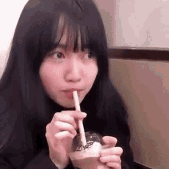 a girl is drinking from a cup with a straw .