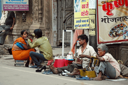 a group of people sit on the sidewalk in front of a sign that says mediterranean food