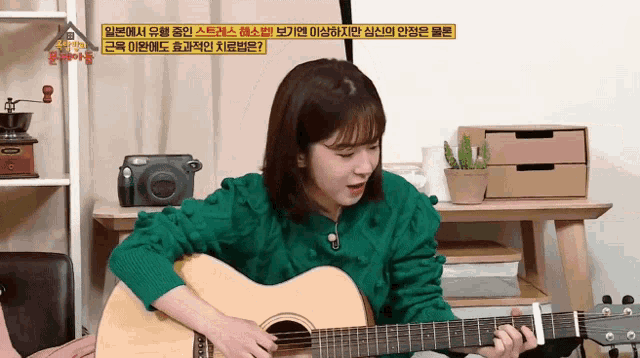 a girl in a green sweater is playing a guitar