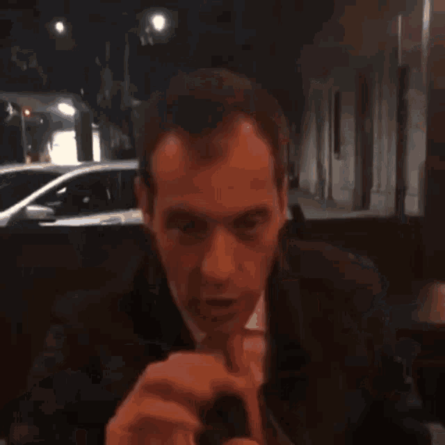a man in a black jacket is standing in front of a building and talking on his cell phone .