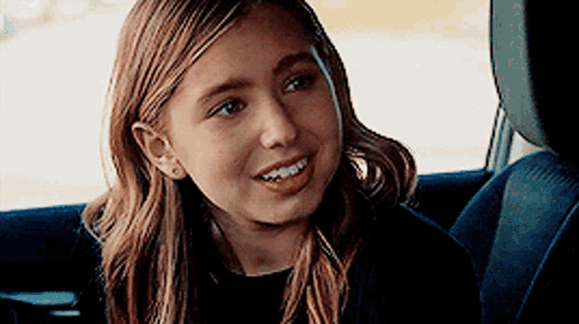 a young girl is smiling while sitting in the back seat of a car .