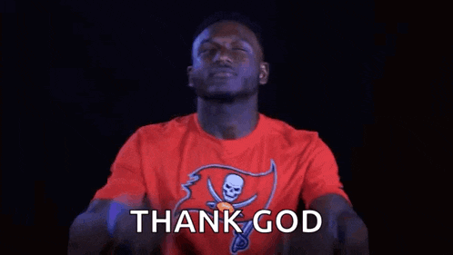 a man in a red t-shirt is pointing up with his fingers and saying thank god .
