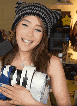 a woman with braces on her teeth smiles while holding a stack of purse straps