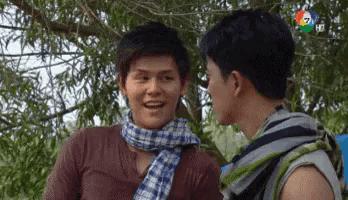 two men are standing next to each other in front of a tree and talking .