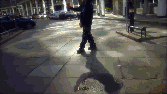 a man walking down a sidewalk with a manhole cover that says habla