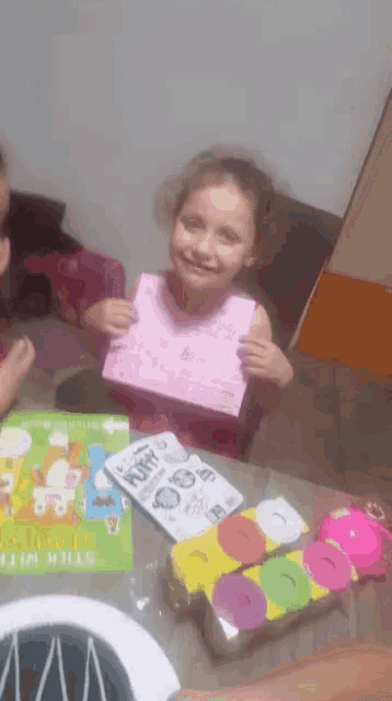 a little girl sitting at a table holding a piece of paper that says fairy on it