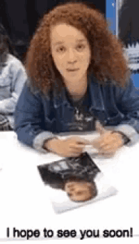 a woman with curly red hair is sitting at a table with a picture of herself on it and the words i hope to see you soon