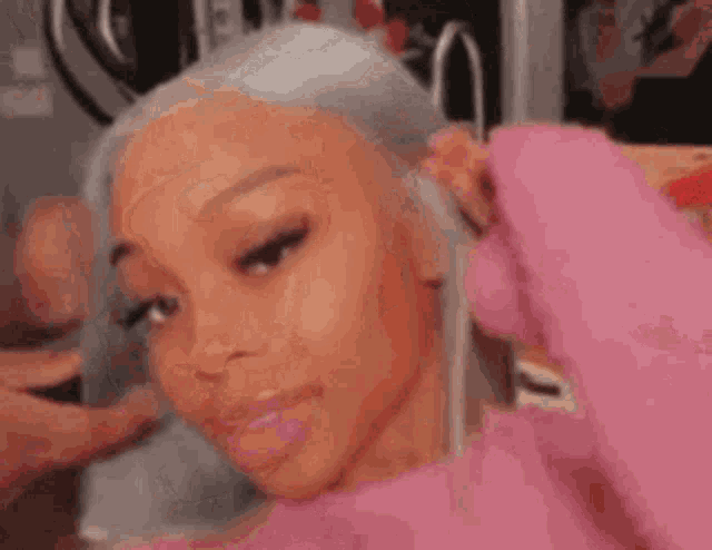 a woman with gray hair is wearing a pink sweater and looking at the camera .