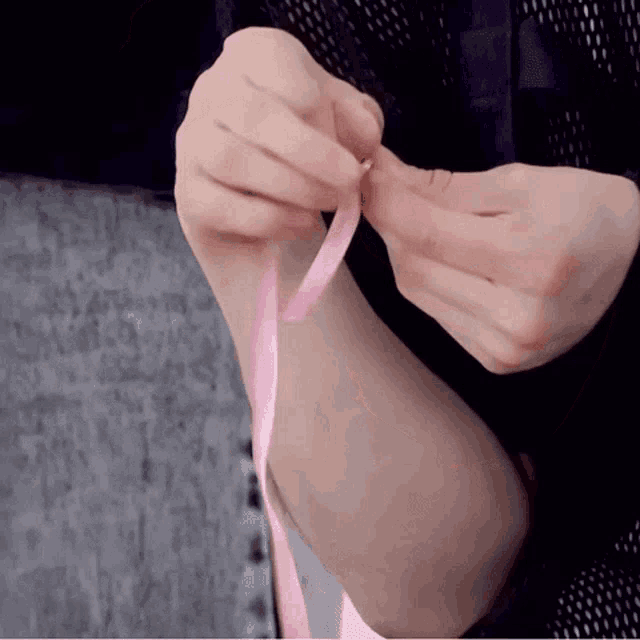 a person is tying a pink ribbon to their wrist