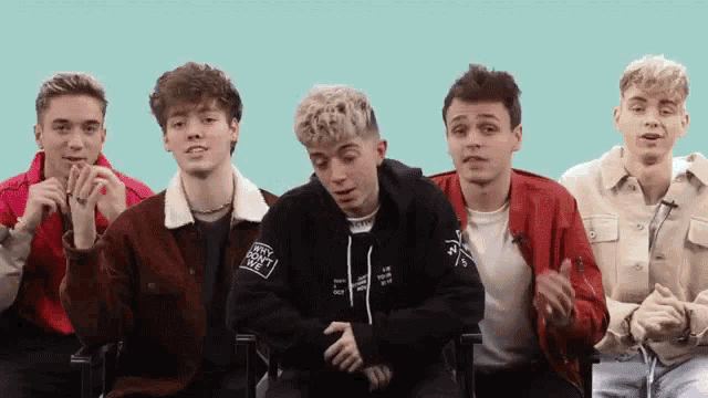 a group of young men are sitting in a row with one wearing a jacket that says why don 't you love me