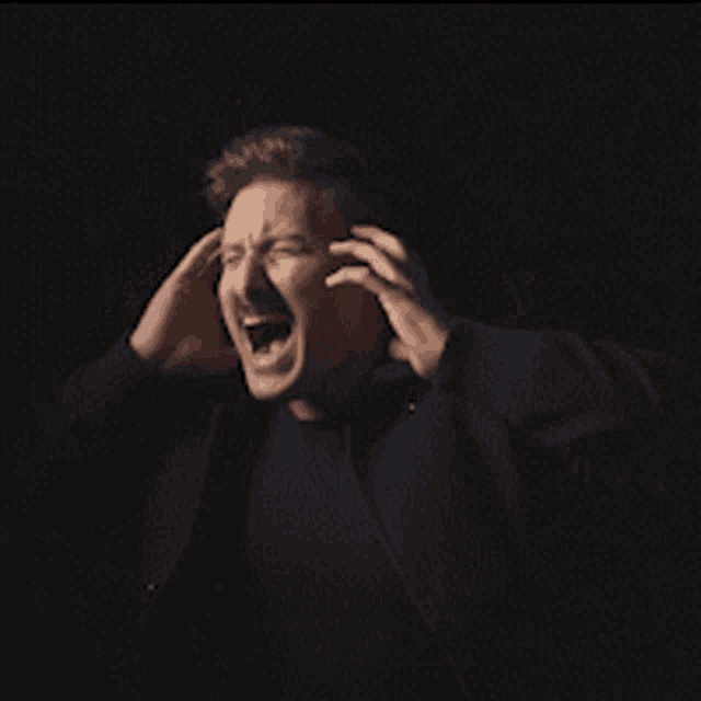 a man with his mouth open is covering his ears with his hands