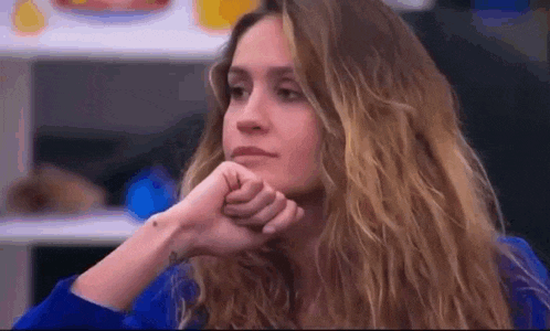 a woman with long blonde hair is sitting with her hand on her chin and looking at the camera .