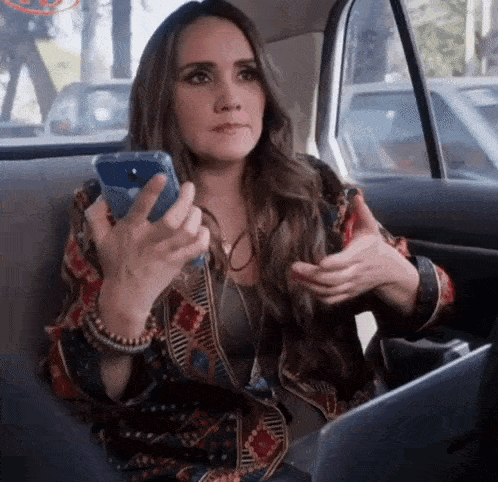 a woman is sitting in the back seat of a car looking at her phone .