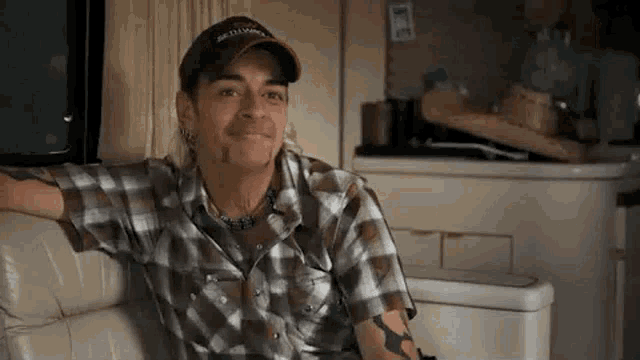 a man in a plaid shirt and hat is sitting on a couch in a trailer .
