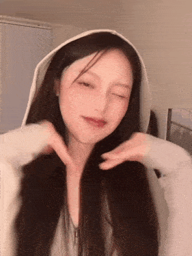 a woman wearing a white hoodie is making a heart shape with her hands .