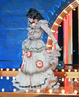 a woman in a long white dress with eyes on it is dancing on a stage