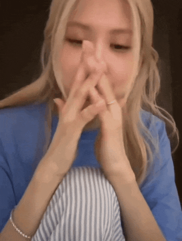 a woman covering her mouth with her hands and wearing a blue shirt