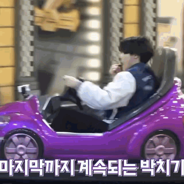 a man is sitting in a purple toy car with chinese writing on the bottom
