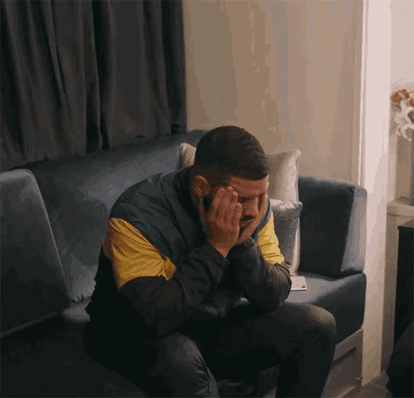 a man is sitting on a couch with his head in his hands