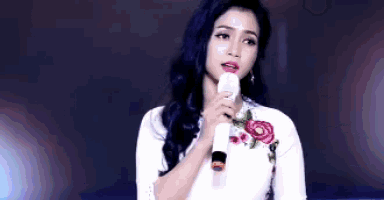 a woman in a white dress is holding a microphone and singing into it .