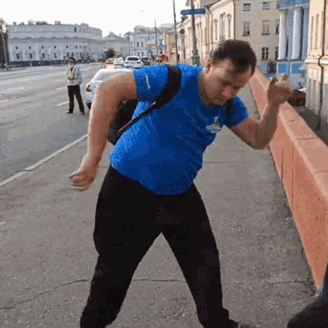 a man in a blue shirt with a backpack on his back is standing on a sidewalk