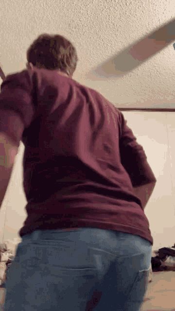 a man in a burgundy shirt and blue jeans is standing in a room .
