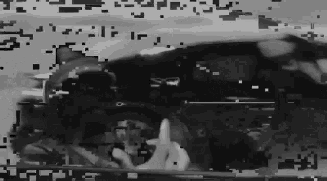 a black and white photo of a person giving the middle finger in front of a car