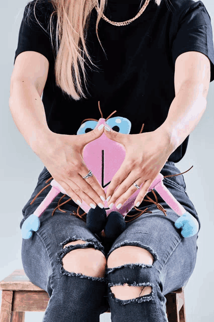 a woman is sitting on a stool holding a stuffed animal with her hands