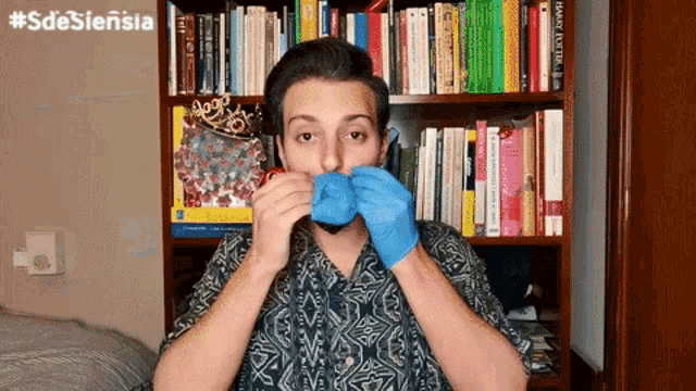 a man wearing blue gloves covering his mouth in front of a bookshelf with harry potter books