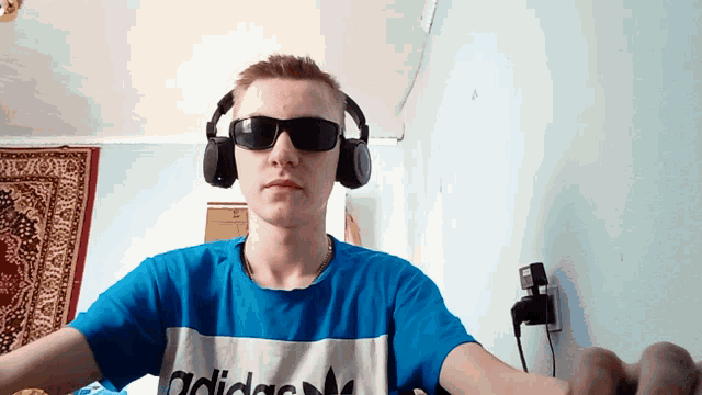 a young man wearing headphones and sunglasses has an adidas shirt on