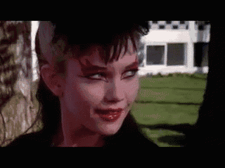 a woman with red makeup on her face is standing in front of a house and looking at the camera .