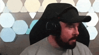 a man with a beard is wearing headphones and a baseball cap while sitting in a chair .