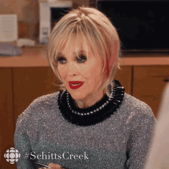 a woman with red lipstick and a sweater that says schitts creek on the bottom