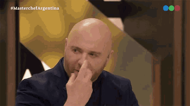 a man in a suit is covering his nose in front of a masterchef argentina logo