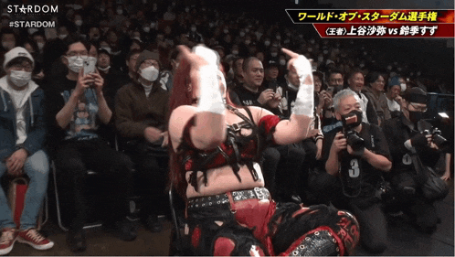 a woman in a red and black outfit is dancing in front of a crowd that is watching a stardom event