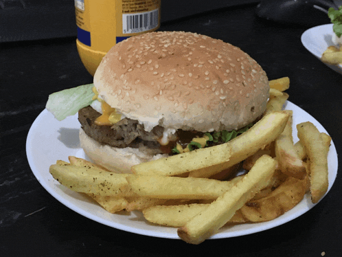 a hamburger and french fries on a plate with a bottle of mustard behind it