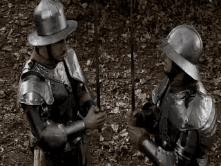 two men in armor are standing next to each other in the woods .
