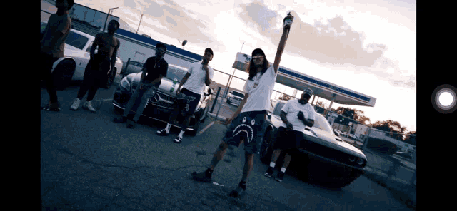 a group of people standing in front of a gas station with a man wearing a sad face shorts