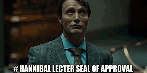 a man in a suit and tie is standing in a dark room and says `` hannibal lecter seal of approval '' .