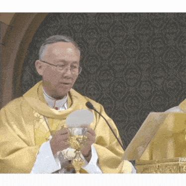 a priest holds a chalice in front of a black wall