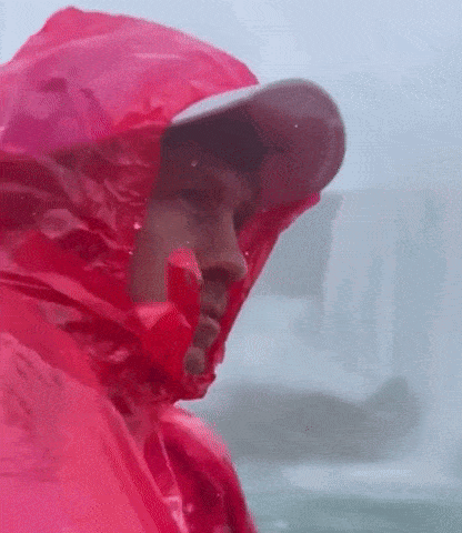 a man is wearing a red raincoat and a hat in the rain .