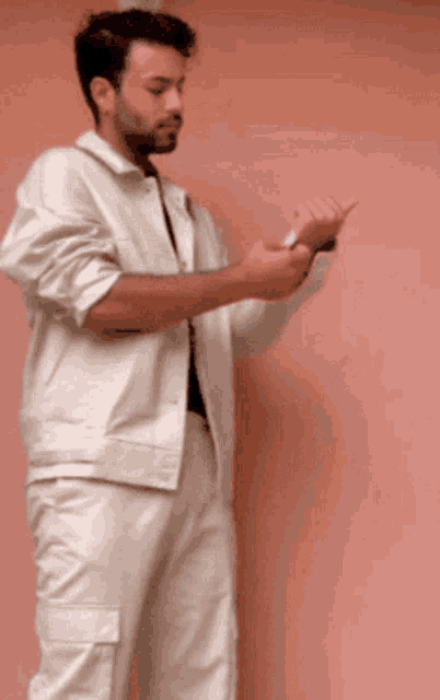 a man wearing a white jacket and pants is standing in front of a pink wall