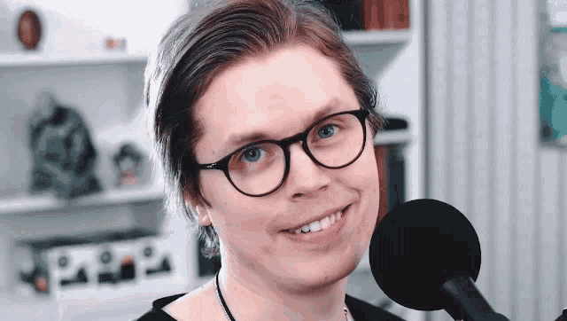 a man wearing glasses is smiling in front of a black microphone