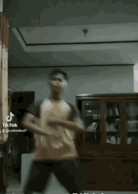 a man in a yellow shirt is dancing in a living room with a tiktok watermark